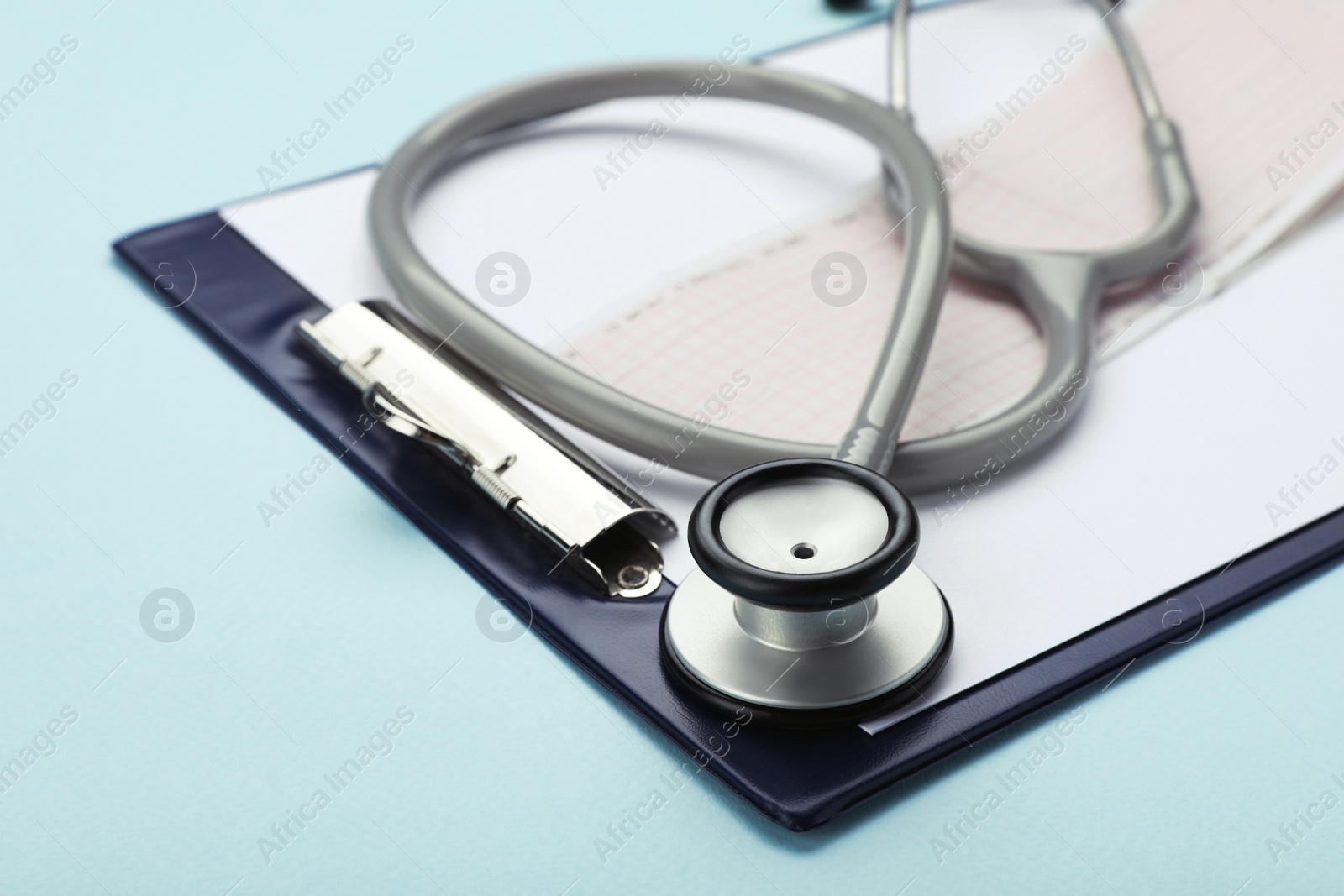 Photo of Clipboard with stethoscope and cardiogram on turquoise background, closeup