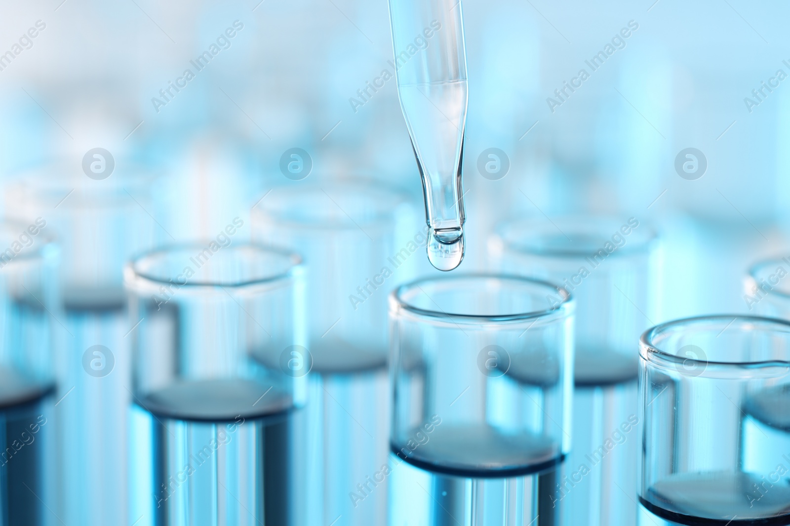 Photo of Dripping liquid from pipette into test tube on light blue background, closeup