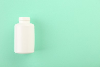 Blank white pill bottle on turquoise background, top view. Space for text