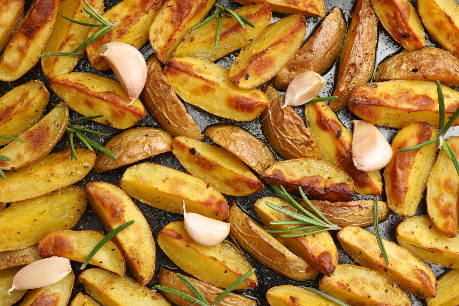 Photo of Delicious baked potatoes with rosemary and garlic on black surface, flat lay