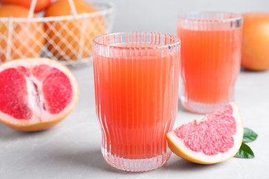 Photo of Tasty freshly made grapefruit juice and fruit on light grey marble table