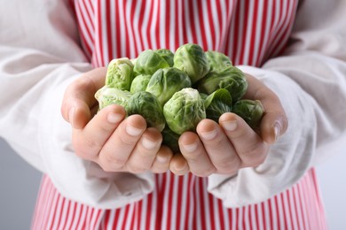 Photo of Woman holding pile of fresh green brussels sprouts, closeup