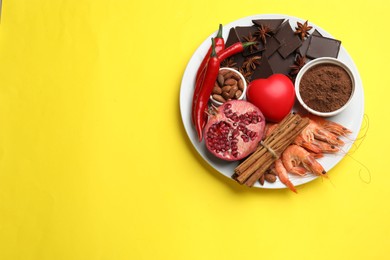 Photo of Natural aphrodisiac. Different products and heart model on yellow background, top view