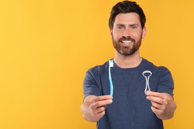 Photo of Happy man holding tongue cleaner and plastic toothbrush on yellow background, selective focus. Space for text