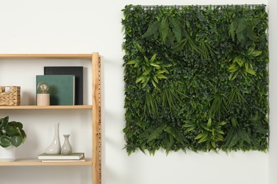 Photo of Green artificial plant panel on white wall and shelving unit with decorative elements in room