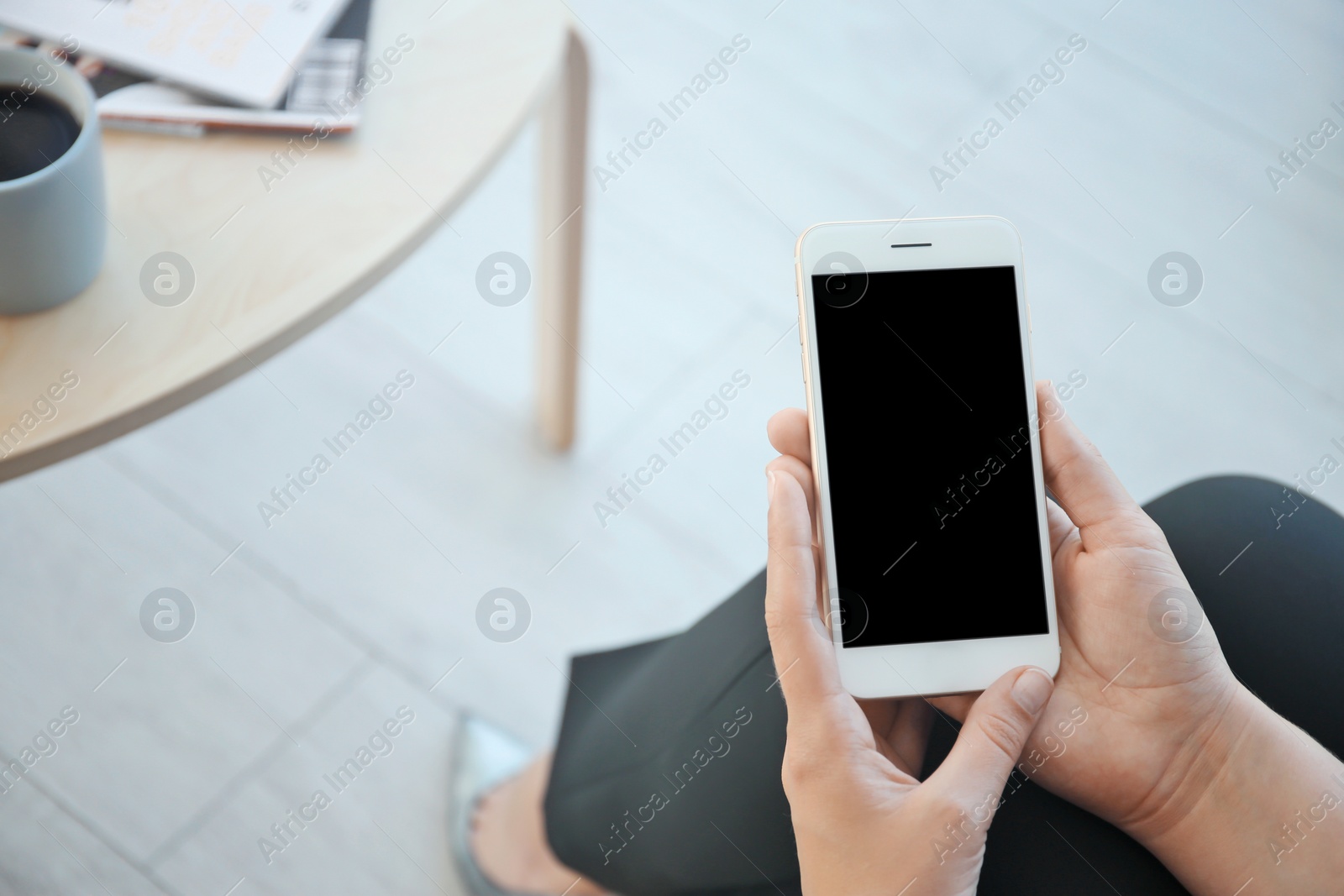 Photo of Young woman holding mobile phone with blank screen in hand indoors