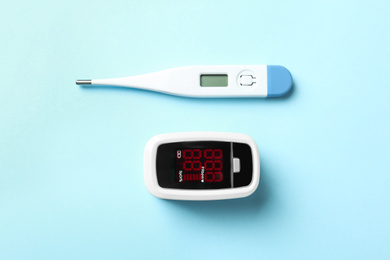 Photo of Modern fingertip pulse oximeter and digital thermometer on light blue background, flat lay