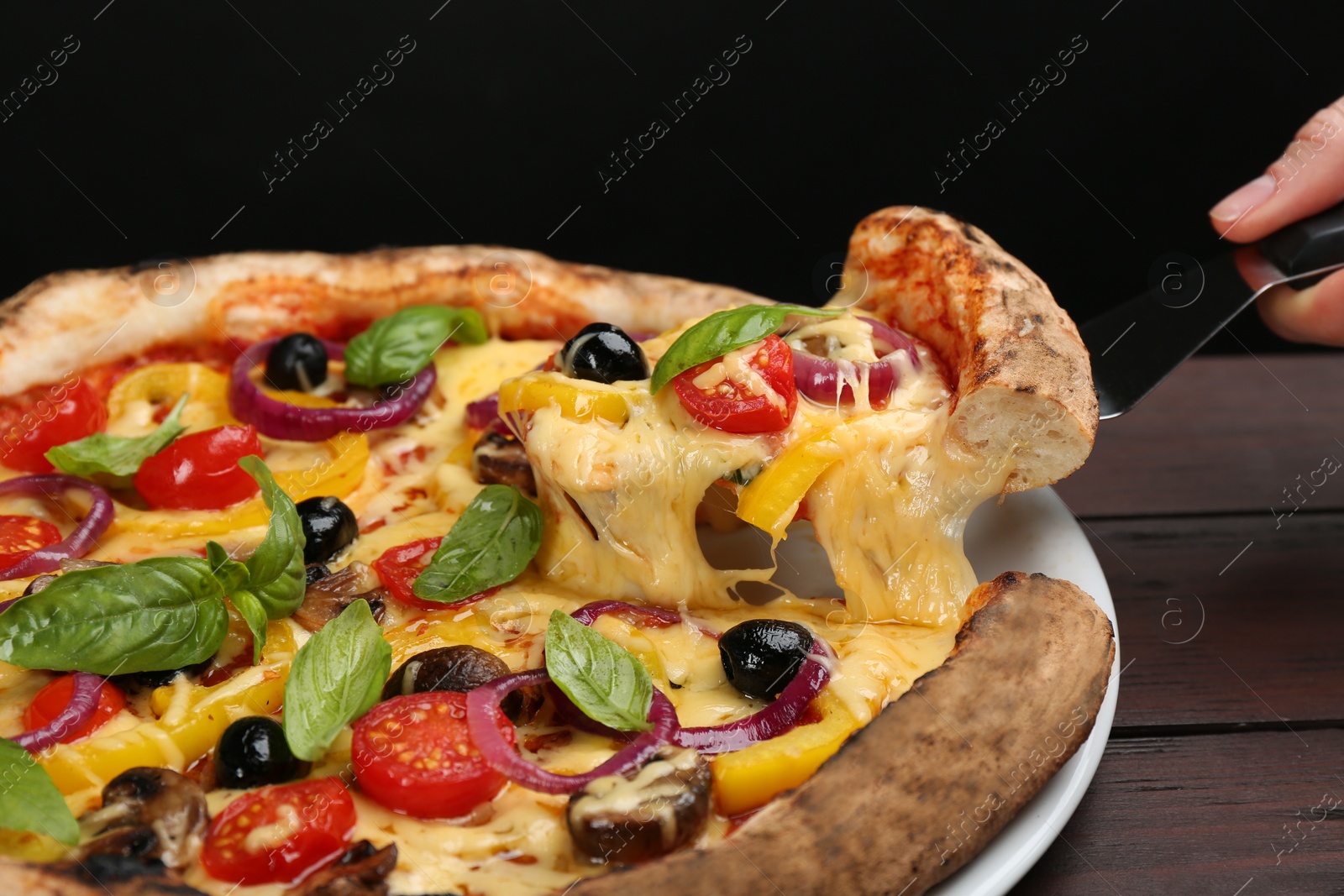 Photo of Woman taking slice of tasty vegetable pizza at wooden table, closeup