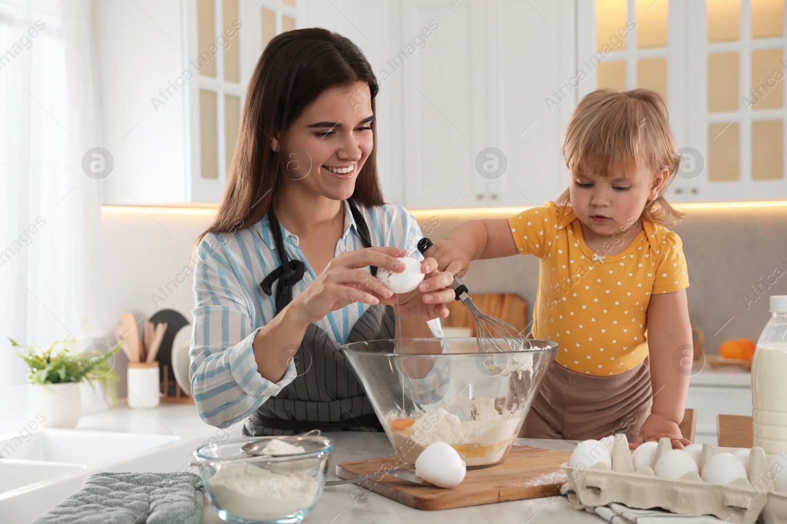 Photo of Mother and her little daughter cooking dough together in kitchen