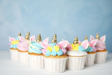Photo of Many cute sweet unicorn cupcakes on white wooden table against light blue background