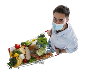 Photo of Young man in medical mask with shopping cart full of groceries on white background, above view