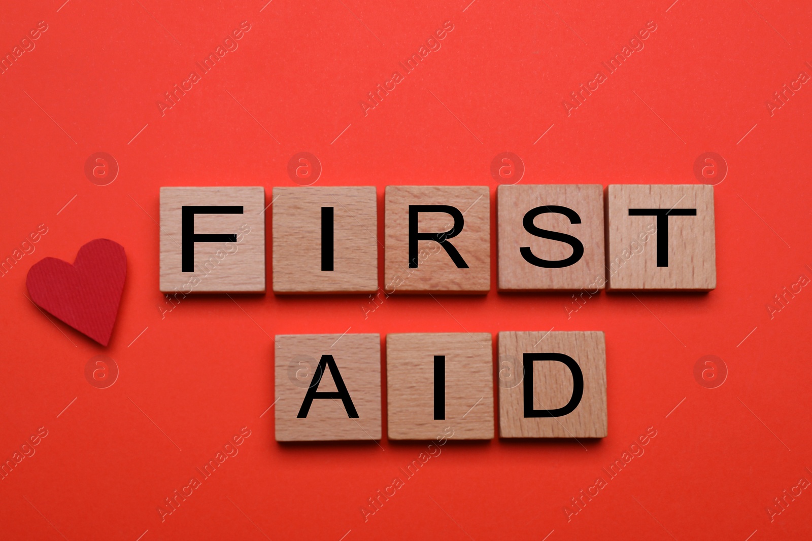 Photo of Words First Aid made of wooden cubes and cardboard heart on coral background, top view