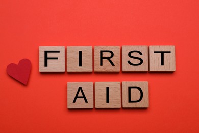Photo of Words First Aid made of wooden cubes and cardboard heart on coral background, top view