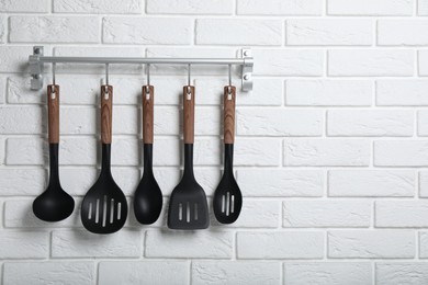 Rack with kitchen utensils hanging on white brick wall. Space for text