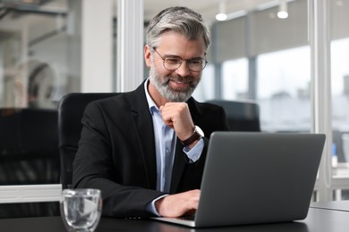 Photo of Smiling man working with laptop at table in office. Lawyer, businessman, accountant or manager