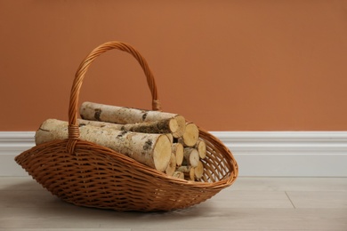 Photo of Wicker basket with firewood near brown wall indoors, space for text