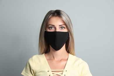 Young woman in protective face mask on light grey background