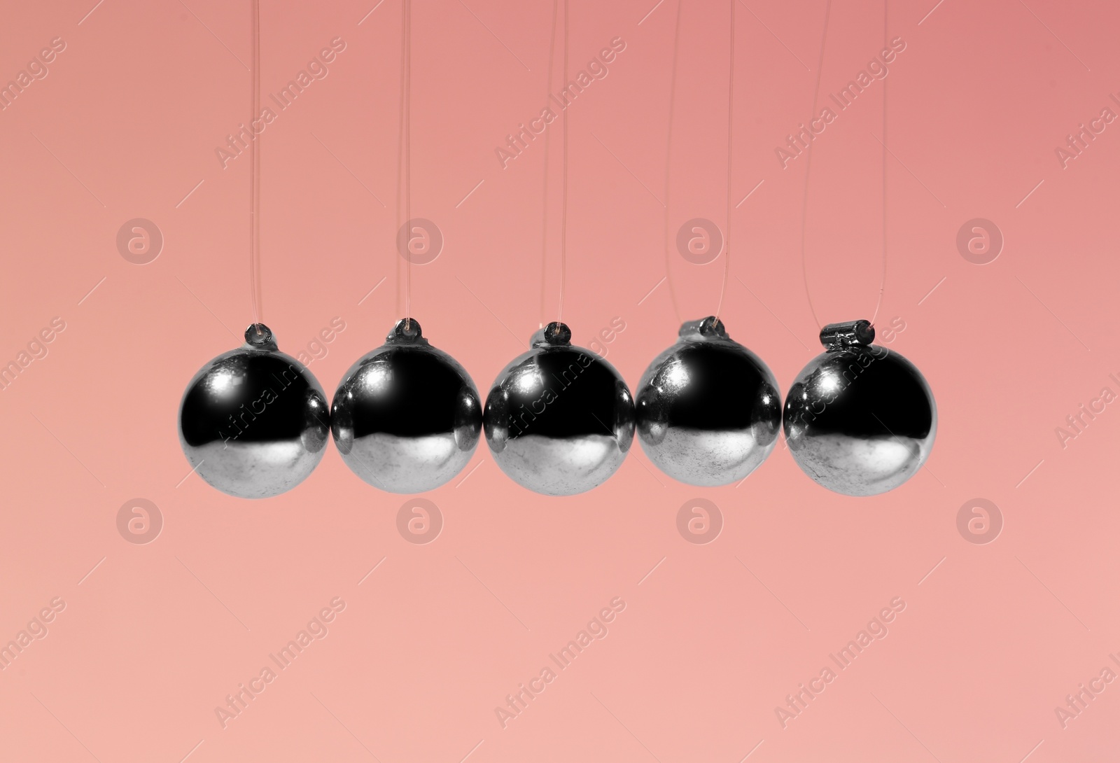 Photo of Newton's cradle on pink background. Physics law of energy conservation