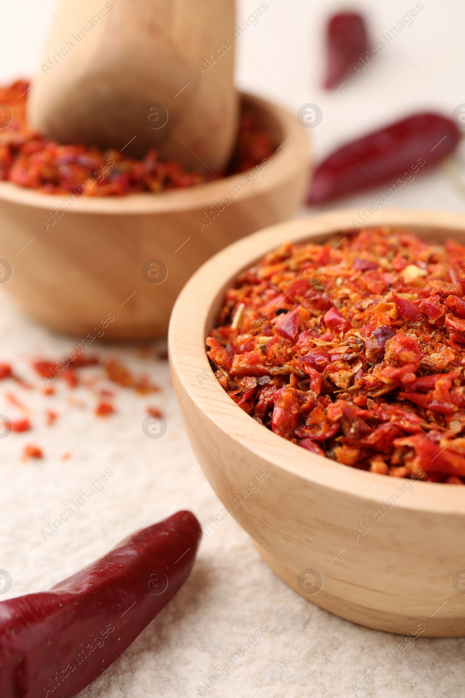 Photo of Chili pepper flakes and pods on light textured table, closeup