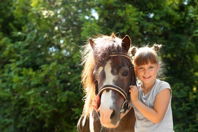 Photo of Cute little girl with her pony in green park
