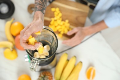 Man adding mango into blender with ingredients for smoothie, top view