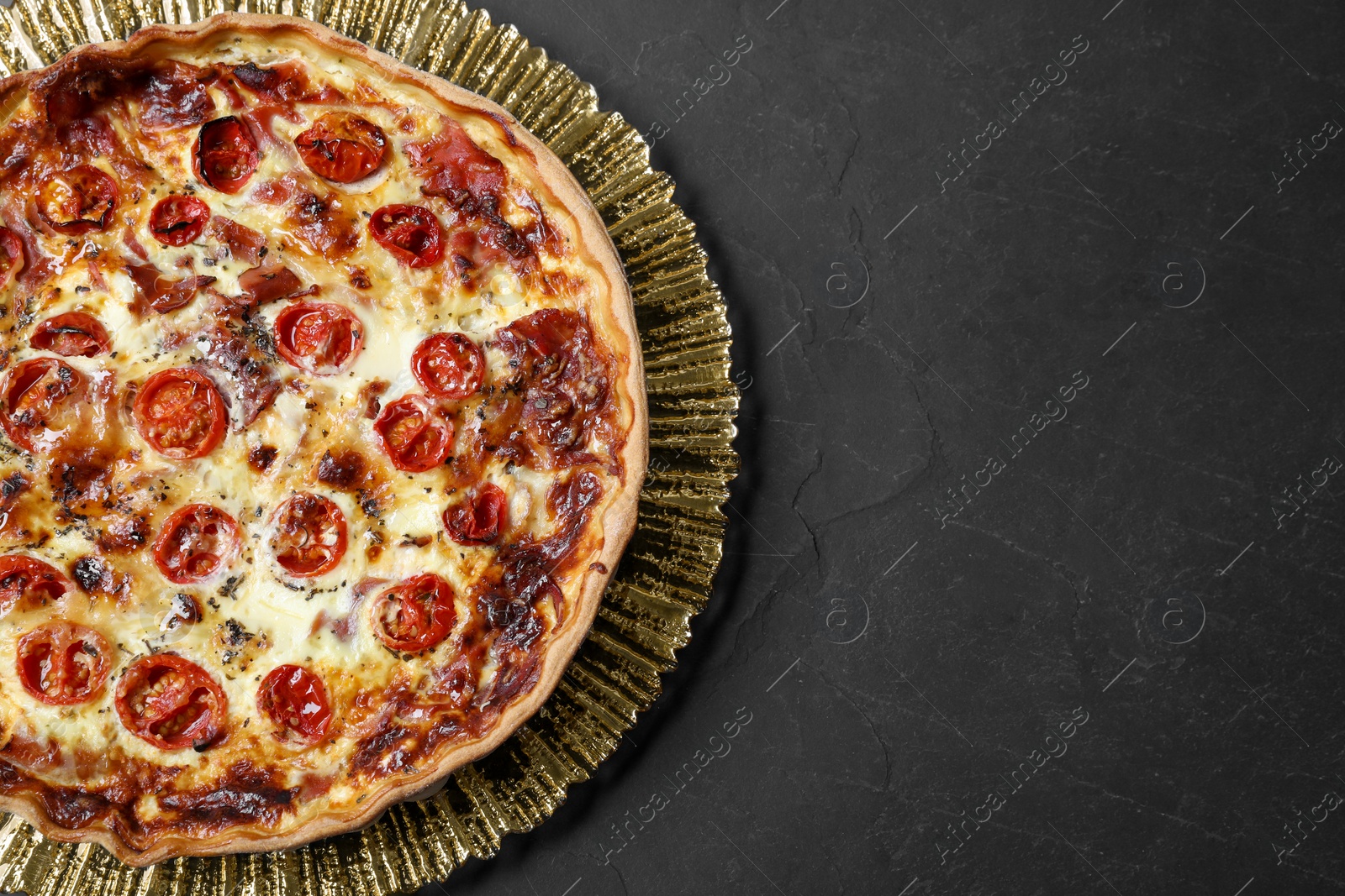 Photo of Delicious homemade quiche with prosciutto and tomatoes on black textured table, top view. Space for text