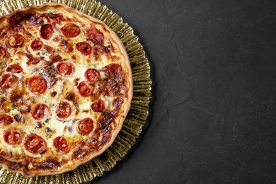 Photo of Delicious homemade quiche with prosciutto and tomatoes on black textured table, top view. Space for text