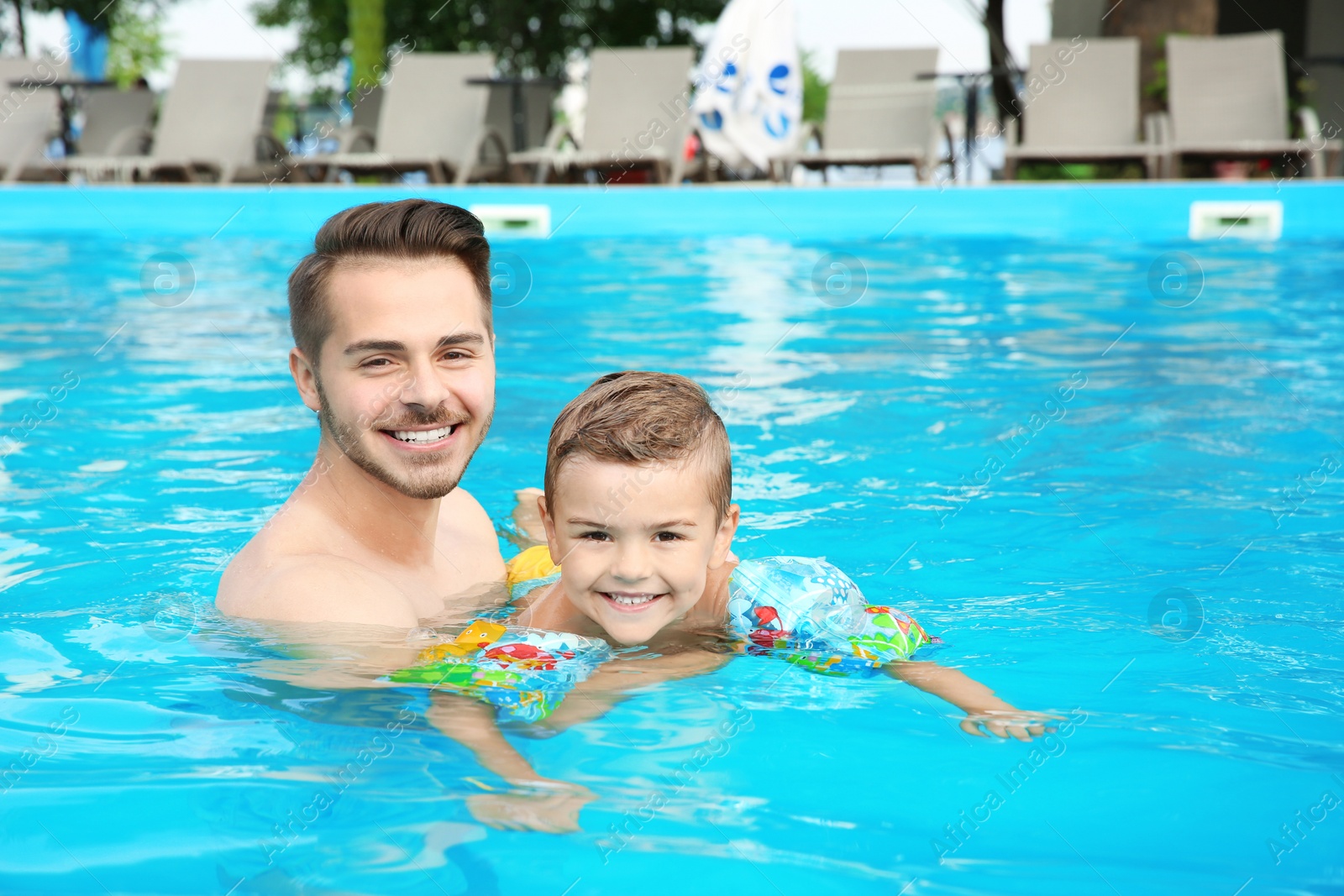 Photo of Father teaching son to swim with inflatable sleeves in pool on sunny day