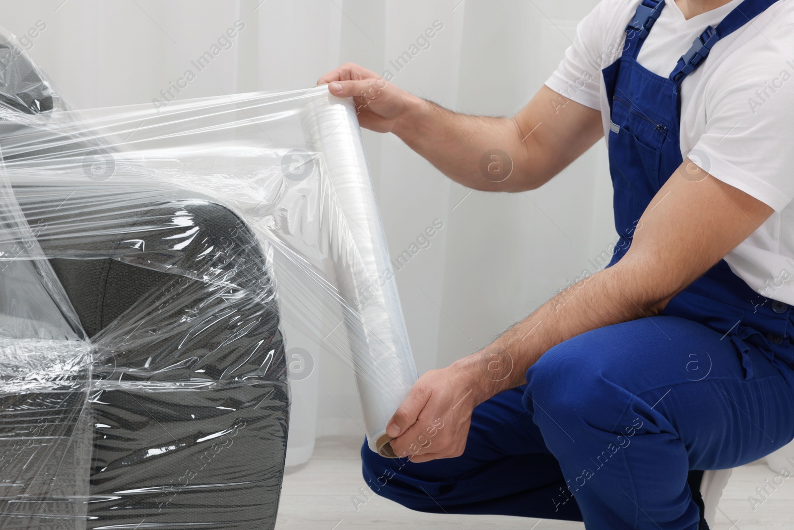 Photo of Worker wrapping sofa in stretch film indoors, closeup