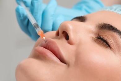 Photo of Doctor giving lips injection to young woman in clinic, closeup. Cosmetic surgery