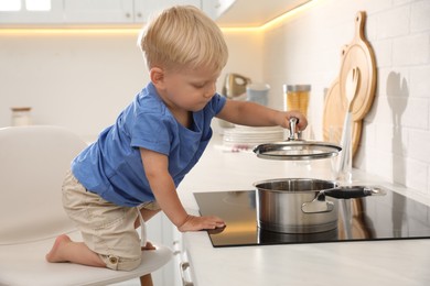 Curious little boy playing with saucepan on electric stove in kitchen