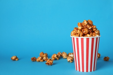 Photo of Caramel popcorn in paper cup on color background. Space for text