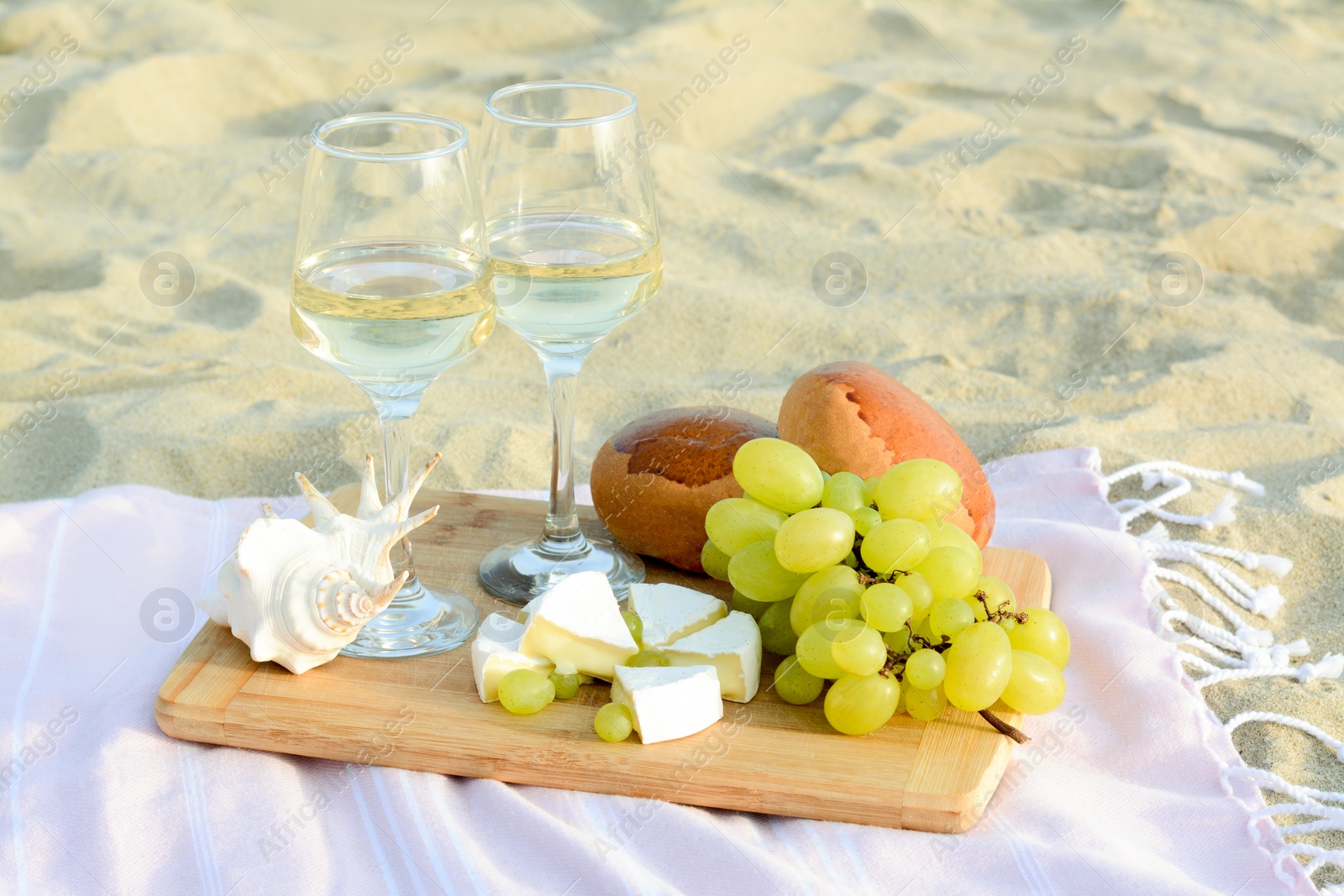 Photo of Glasses with white wine and snacks for beach picnic on sand outdoors