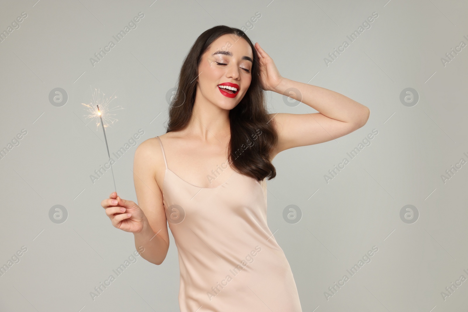 Photo of Christmas celebration. Beautiful young woman with sparkler on grey background