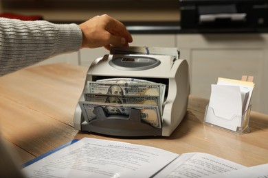 Photo of Man putting money into banknote counter at wooden table indoors, closeup