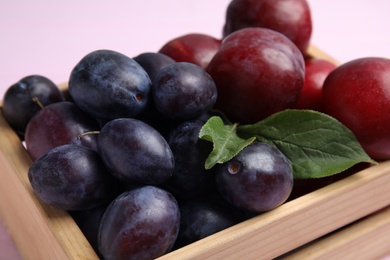 Photo of Delicious ripe plums in crate on pink background, closeup