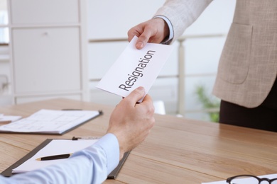 Photo of Employee giving resignation letter to boss in office, closeup