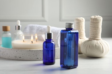 Photo of Spa composition. Bottles of cosmetic products, herbal bags, towel and burning candle on light table