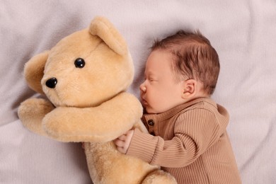 Photo of Cute newborn baby sleeping with toy bear on blanket, top view
