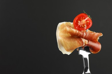 Fork with slice of tasty jamon and tomato on black background, closeup. Space for text