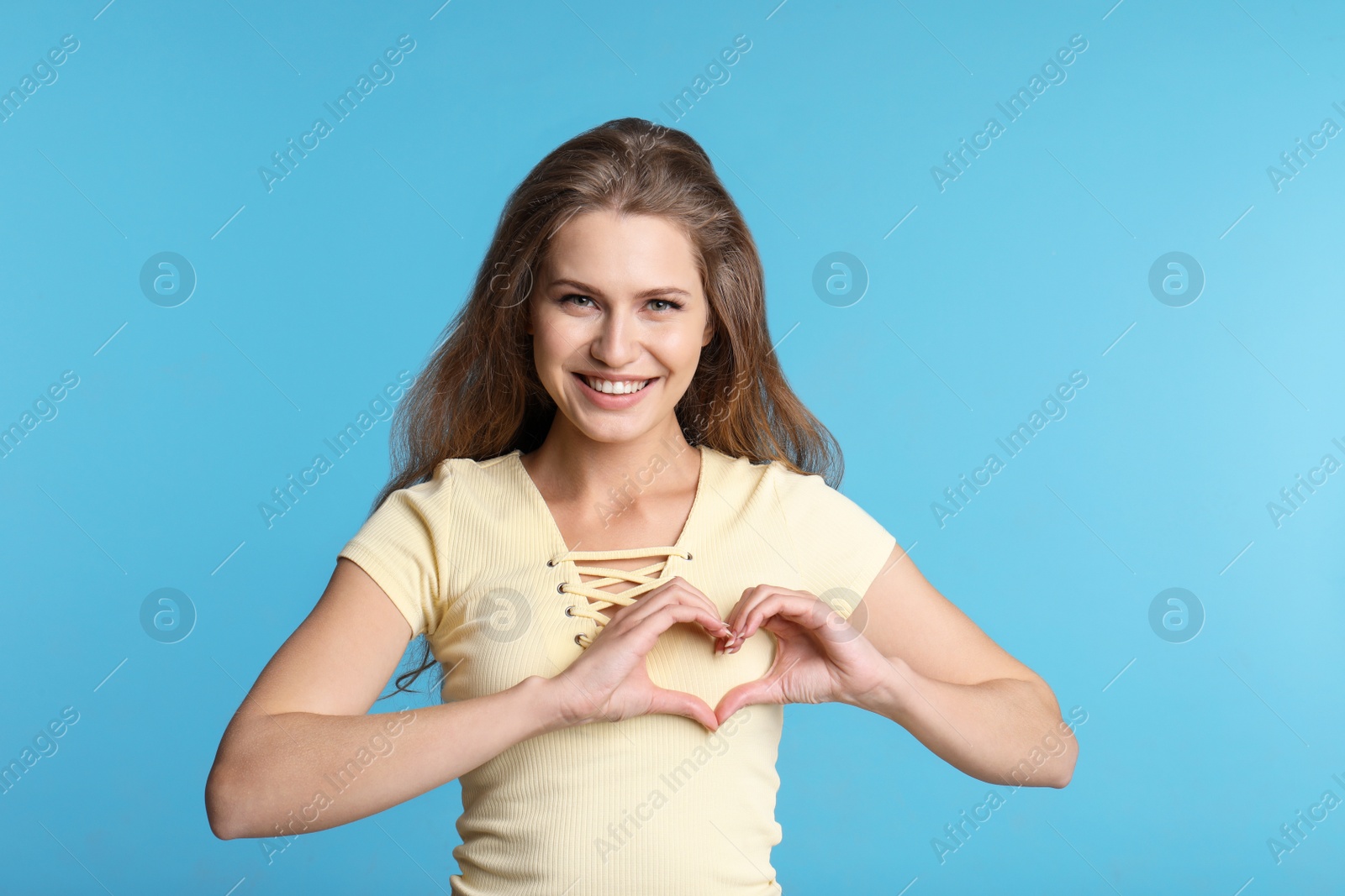 Photo of Woman making heart with her hands on color background