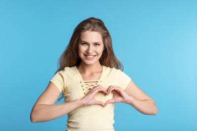 Woman making heart with her hands on color background