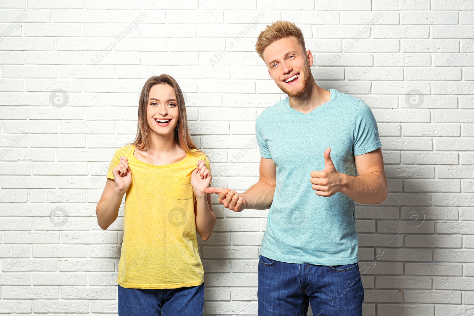 Photo of Young couple wearing blank t-shirts near white brick wall. Mockup for design