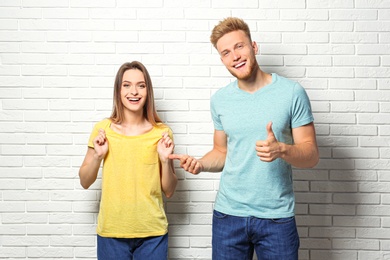 Photo of Young couple wearing blank t-shirts near white brick wall. Mockup for design