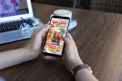 Photo of Woman reading online magazine on mobile phone at wooden table, closeup