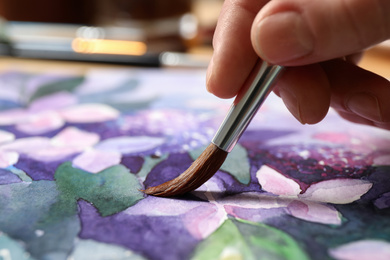 Photo of Woman painting beautiful flowers with watercolor, closeup