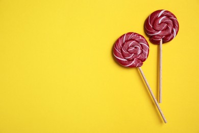 Sticks with bright lollipops on yellow background, flat lay. Space for text