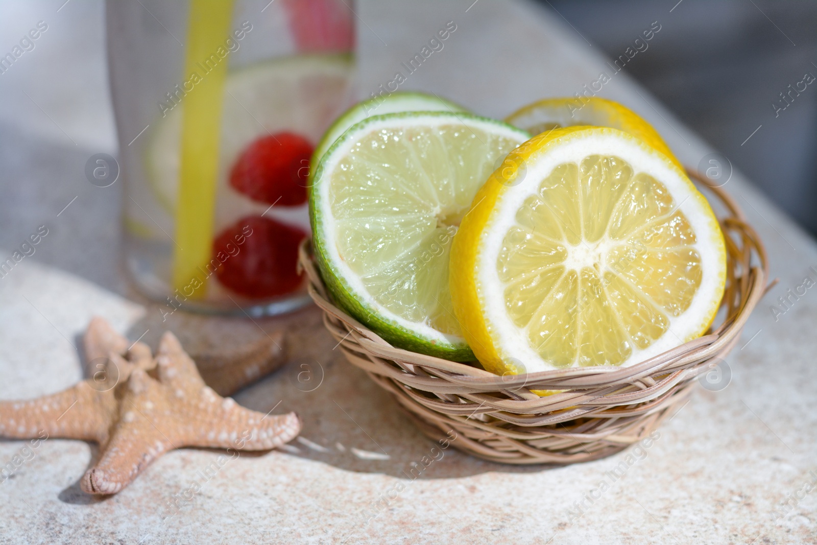 Photo of Citrus fruits and refreshing tasty lemonade served in glass bottle on beige table, closeup