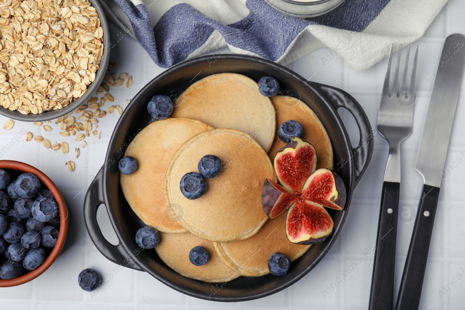 Photo of Tasty oatmeal pancakes and ingredients on white tiled table, flat lay