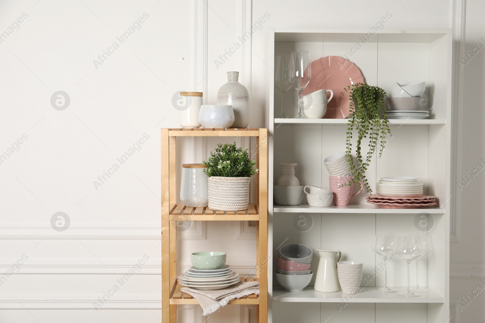 Photo of Different clean dishware and houseplants on shelves in cabinet indoors